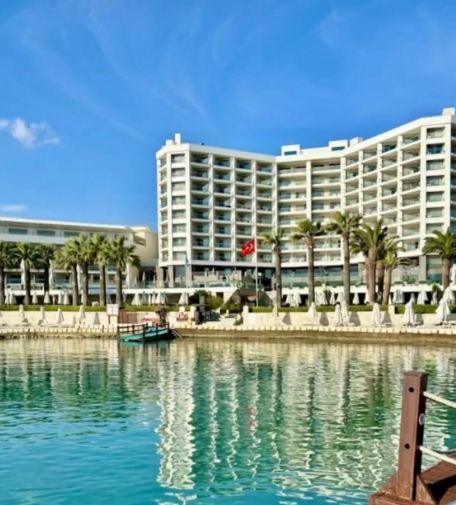 Otel binası, palmiyeler ve önündeki sakin lagünün yansıması