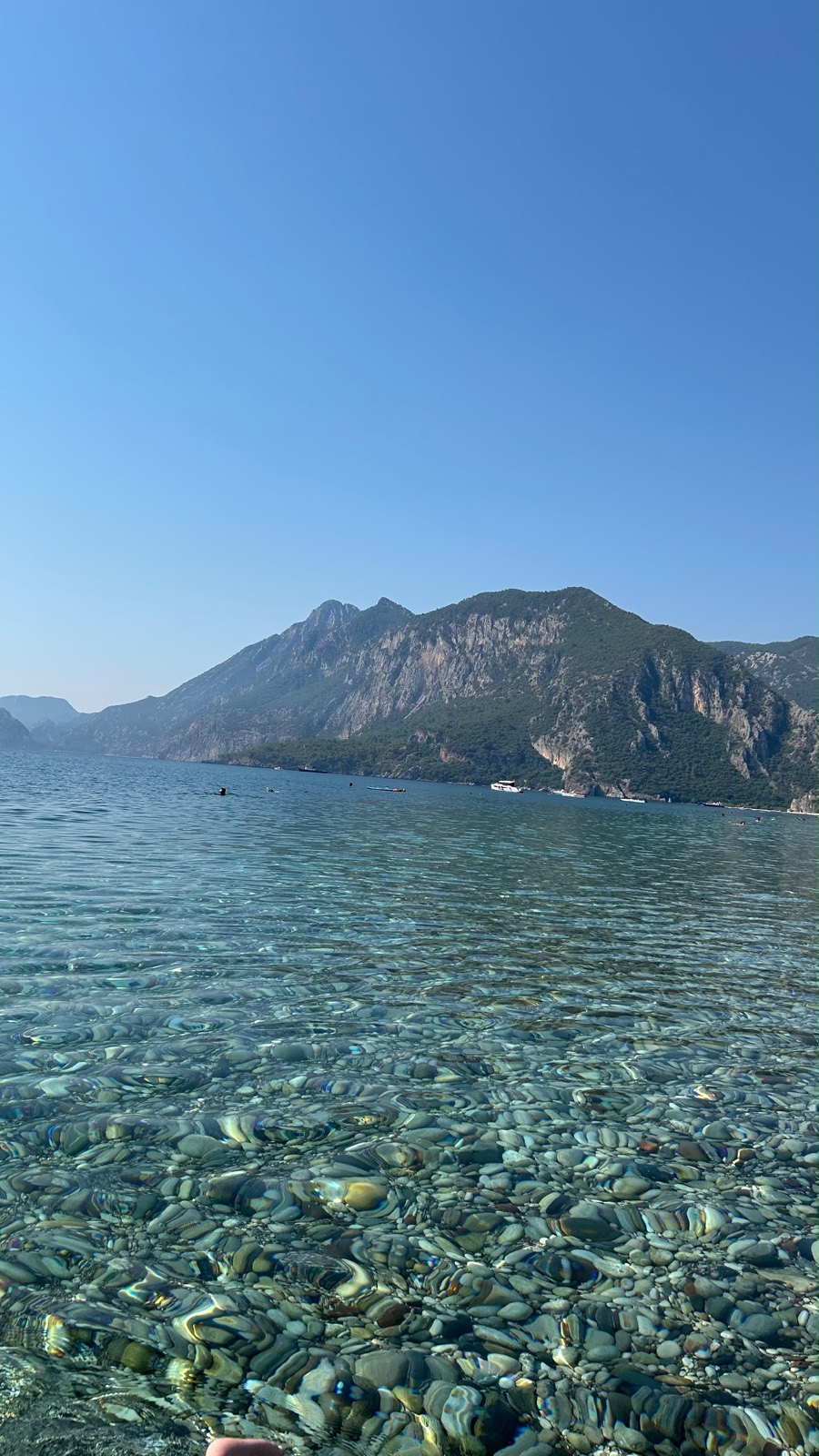 Çıralı'da berrak, çakıllı deniz ve arkada yeşil dağlar