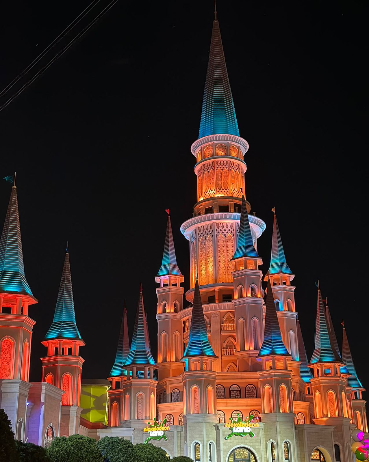 The many-spired Nickelodeon Land castle lit in orange and turquoise at night