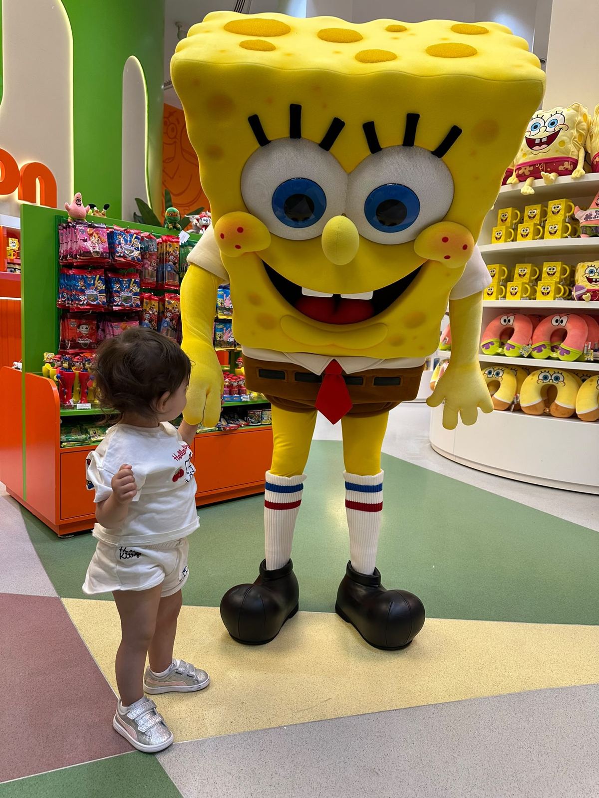 A small child holding the hand of a giant SpongeBob mascot in the store, back to the camera