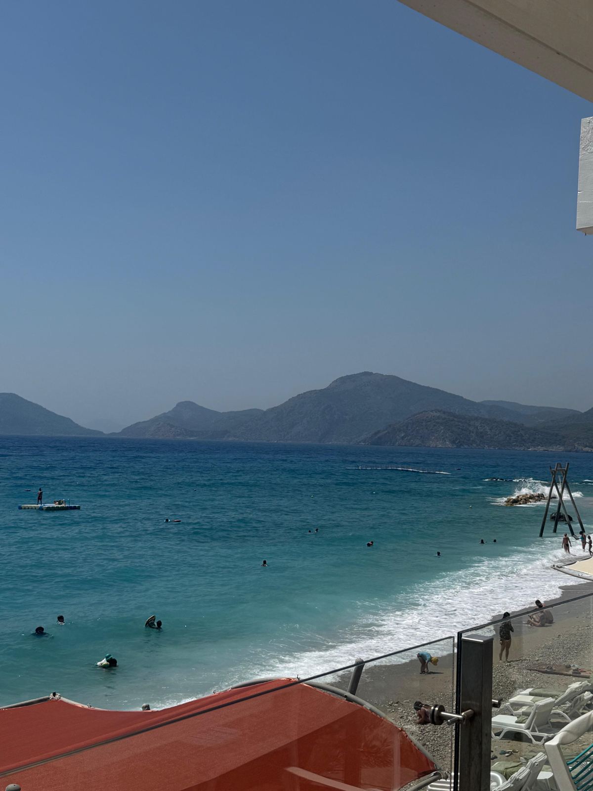 Yüksekten koy manzarası: dalgalı deniz, çakıllı sahil ve karşıda tepeler