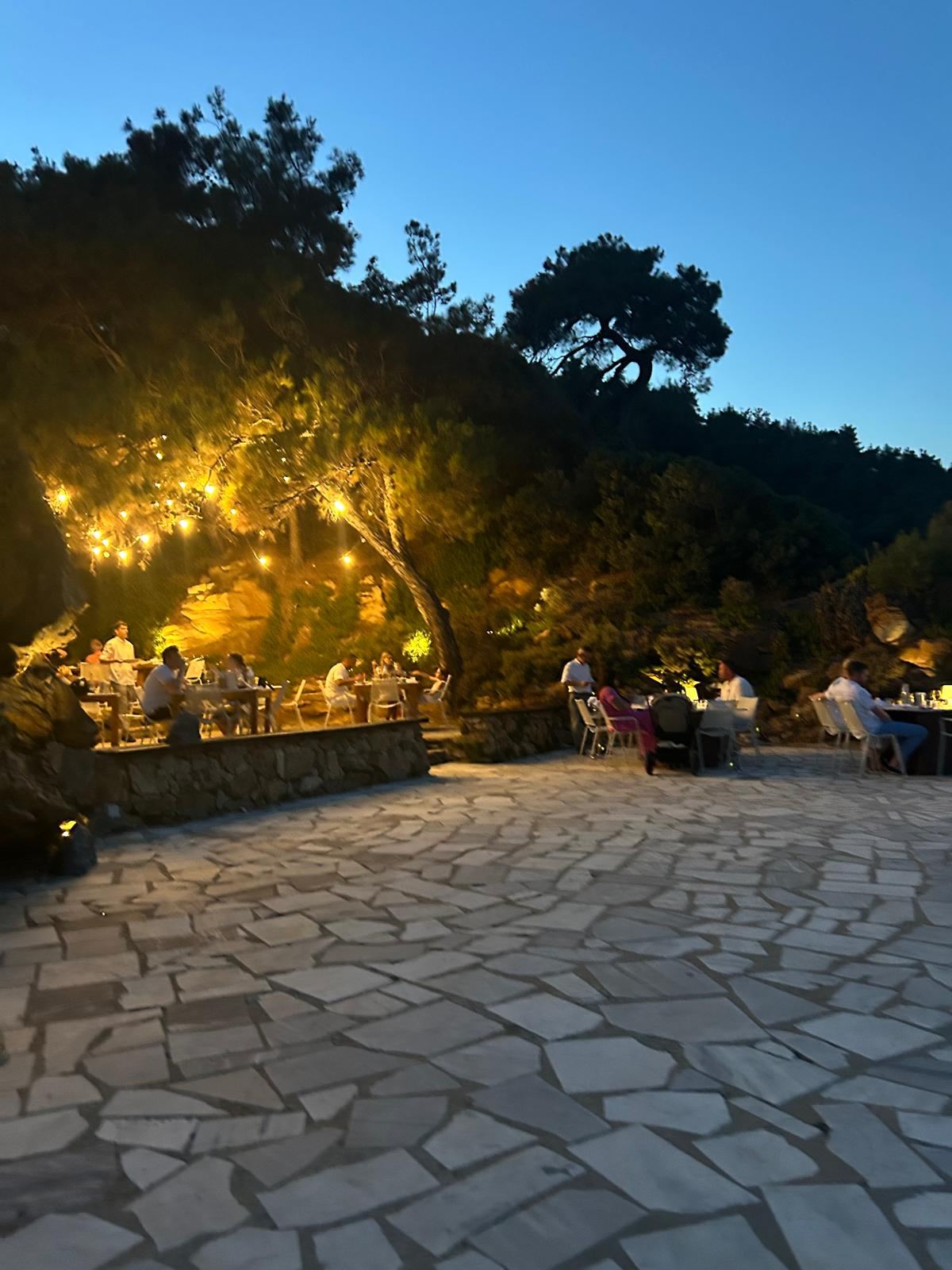 Akşam saatinde kayaların üzerine kurulu, ağaçlara asılı ışıklarla aydınlatılmış açık hava restoranı