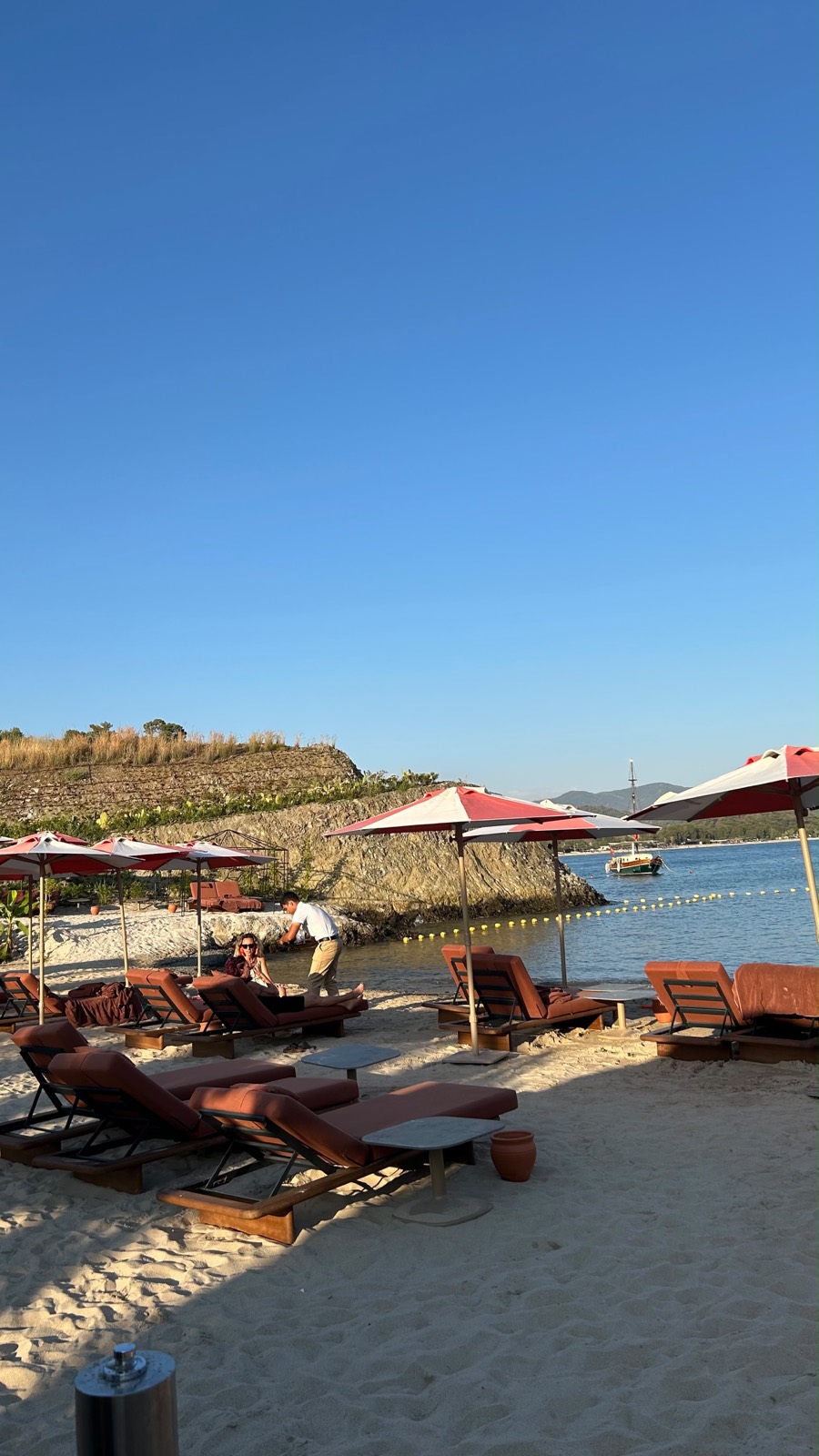 Kum plajda kırmızı-beyaz şemsiyeler, şezlonglar ve deniz